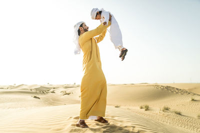 Woman standing on sand dune in desert against clear sky