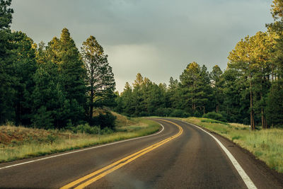 Country road amidst trees against sky