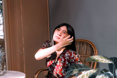 Portrait of young woman with hand in hair while sitting on chair at home