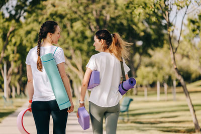 Two young women walking in the morning park. carrying mats and other equipment for yoga.