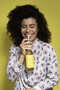 Smiling young woman holding drink against yellow background