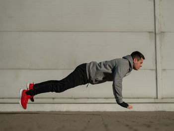 Side view of young man sitting on wall