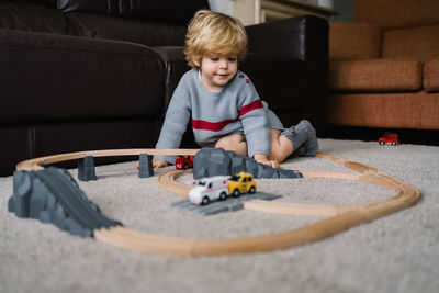 Curly haired little kid playing with toy road and cars on carpet at home