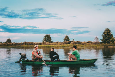 People sitting on boat in lake against sky