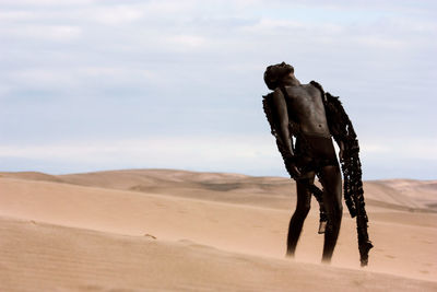 Teenage boy in costume on desert against sky