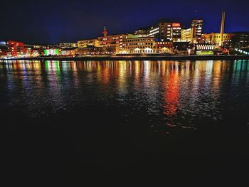 Illuminated buildings by river against sky at night