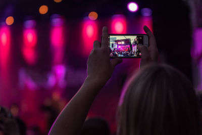 Midsection of woman photographing illuminated smart phone at music concert