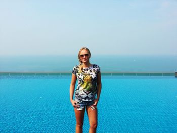 Portrait of beautiful woman standing at swimming pool standing against sea