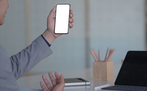 Midsection of person holding mobile phone at table