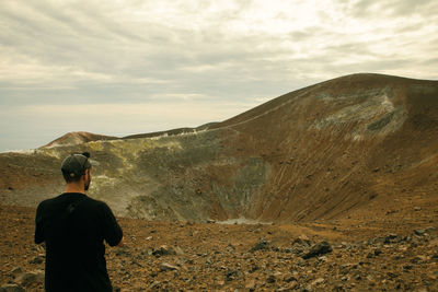 Rear view of man standing on mountain against sky