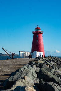 Lighthouse by sea against clear blue sky