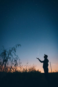 Silhouette man standing on field against sky at night catching a shooting star
