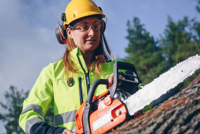 Female worker cutting tree trunk with electric saw