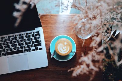 High angle view of coffee cup with laptop and flowers on wooden table