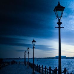 Silhouette street light by sea against blue sky