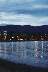 Illuminated buildings by sea against sky at night