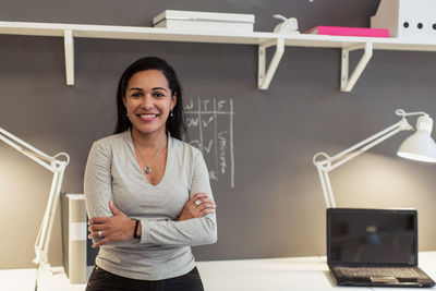 Portrait of confident businesswoman with arms crossed standing against wall at creative office