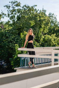 Beautiful young woman standing on balcony against trees