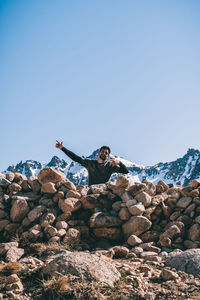 Low angle view of man standing on rock against clear blue sky