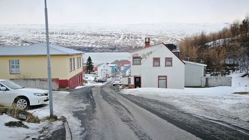 Snow covered road by buildings in city