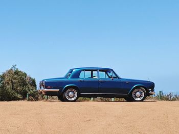 Vintage car on field against clear blue sky