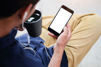 Low section of man with coffee cup using phone while sitting at home