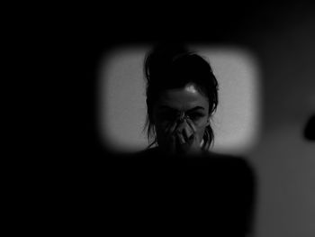 Woman covering face while standing against wall at home