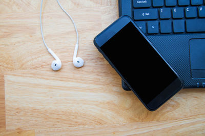 High angle view of mobile phone and laptop by headphones on wooden table