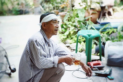 Side view of mature man having drink while crouching at yard