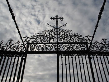 Low angle view of gate against cloudy sky