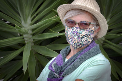 Close-up portrait of senior woman wearing mask sitting against plant