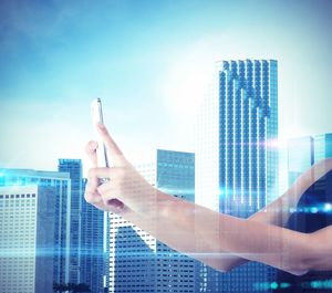 Midsection of person using mobile phone against modern buildings in city