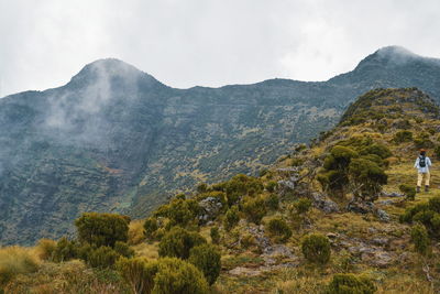 Woman walking on mountain against sky