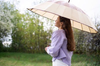 A girl in a sweater is standing under an umbrella. it's raining person