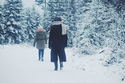 Rear view of women walking on snow covered forest