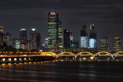 Illuminated city by river against sky at night