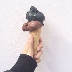 Cropped hand of person holding ice cream against white wall