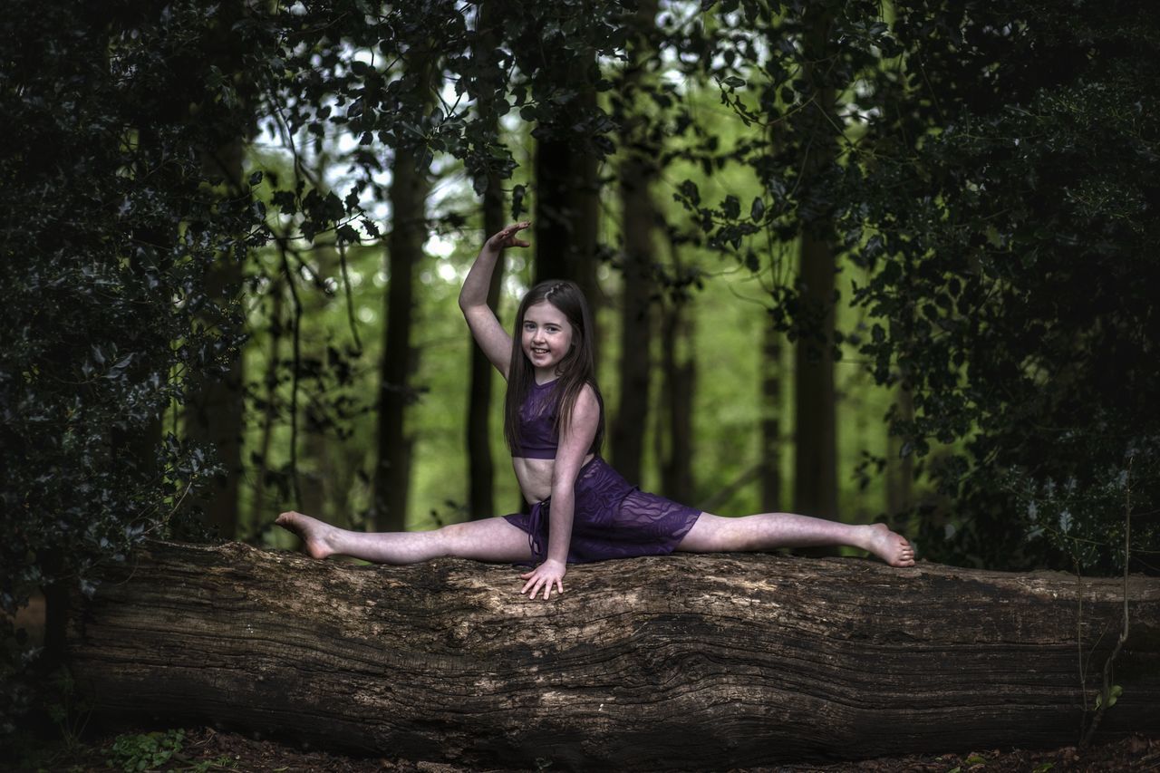 tree, plant, one person, young adult, leisure activity, full length, real people, young women, nature, lifestyles, women, casual clothing, day, forest, front view, human arm, growth, tree trunk, outdoors, wood, beautiful woman, hairstyle, arms raised