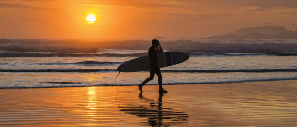 Silhouette woman standing at beach against sky during sunset