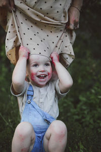 Playful son pulling mother's clothes while crouching in yard