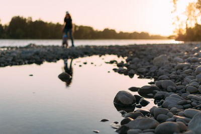 Full length of person with pebbles at beach against sky during sunset