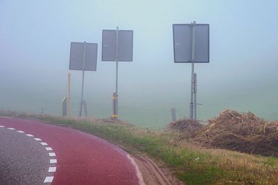 Road sign on grass against sky