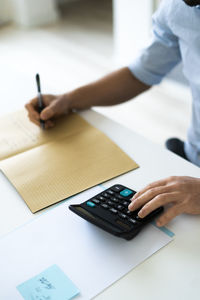 Businessman writing in book while using calculator at office