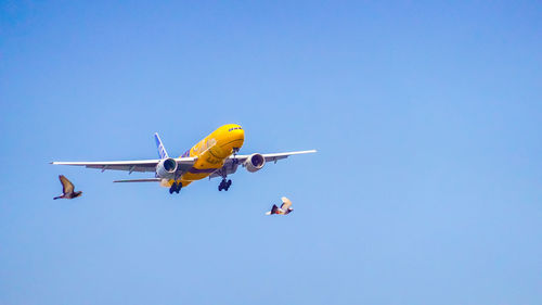 Low angle view of airplane flying against clear blue sky