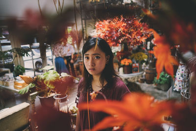 Portrait of young woman standing by potted plants