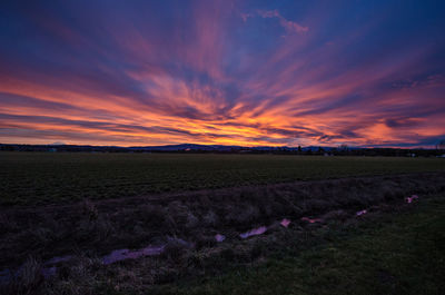 Scenic view of field against dramatic sky during sunset