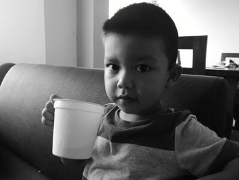 Close-up portrait of boy having drink on sofa at home