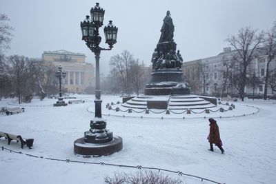 Woman walking on snow by catherine the great monument in city during winter