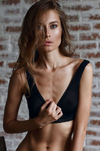 Portrait of sensuous woman touching bra against brick wall