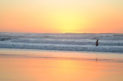 Silhouette man standing on beach against sky during sunset